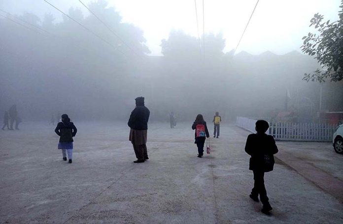 Children are on the way to school during thick fog that engulfs the whole city during morning time