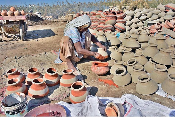 An elderly woman is painting clay pots at Kumhar Para