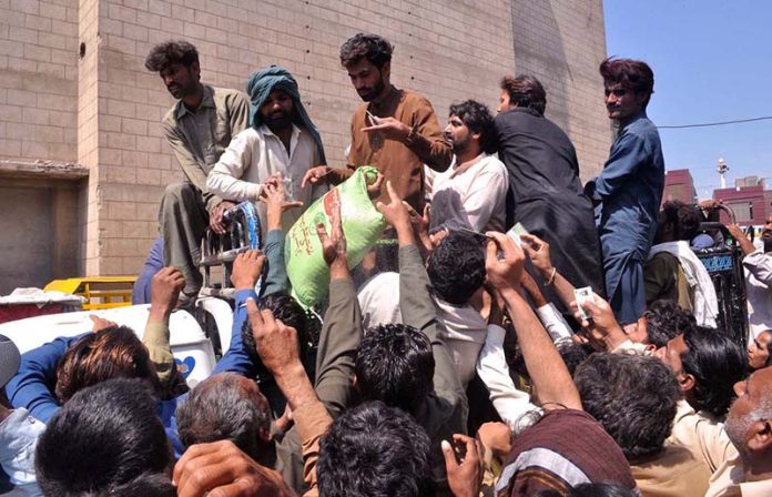 People receive free flour bags from a distribution point under Prime Minister’s Ramazan package for deserving families at Sattelite Town