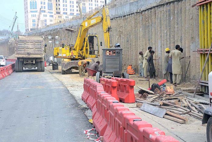 Heavy machinery being used for a road construction work while laborers are busy in finishing after concrete framework removal near Liberty Market