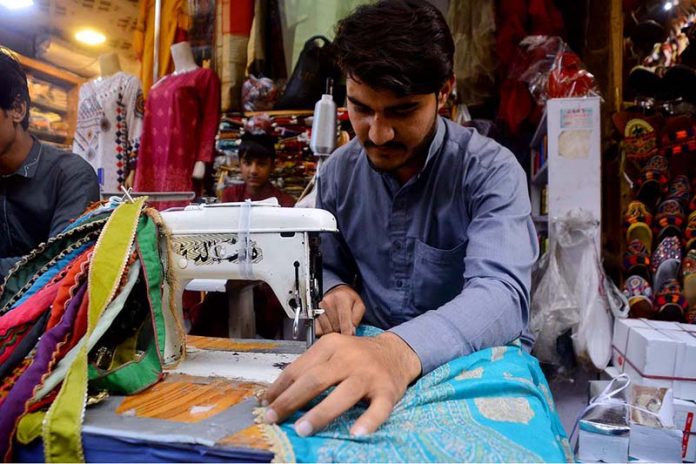 Tailor busy in pico on dupatta at his workplace in Kali Bari Area.