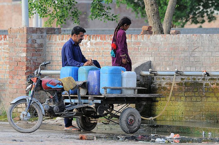 A person with his daughter filling their cans with water from the water pipeline at Fatima Jinnah Town