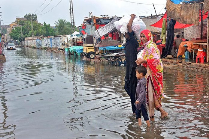 People passing through rain water accumulated at Railway Colony area after heavy rain in the city