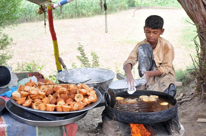 A young vendor frying a traditional sweet item (Aam rasay) for the customers at his roadside setup