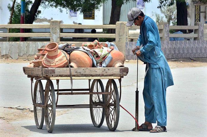 A vendor is pumping air into the tire of hand cart by using hand pump at Latifabad