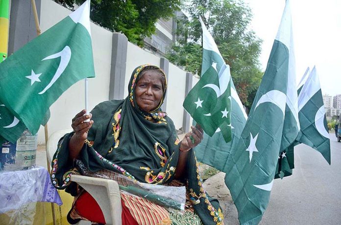 A woman displays national flags ahead of Independence Day Pakistan at her roadside stall