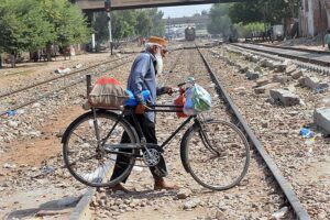 An elderly person along with bicycle crossing rail track while a train approaching on the same track may cause any mishap