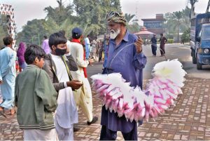 An elderly vendor selling cotton candy (Lacha) while shuttling on road.