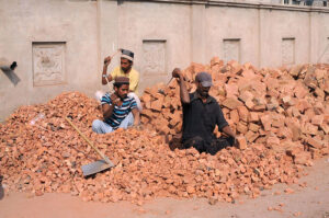 Labourers crushing bricks into pieces for construction use.