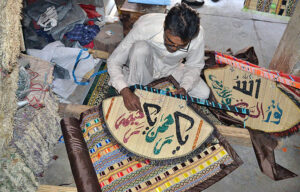 A skilled worker is writing the Qur'anic verse on a hand fan