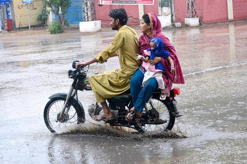 A family traveling on the motorcycle under the cover of umbrella to protect from rain in the city.