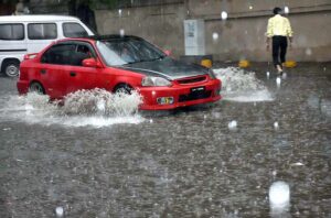 A person pushing his cycle sitting on a kid passing through rain water accumulated during heavy rain in the city.