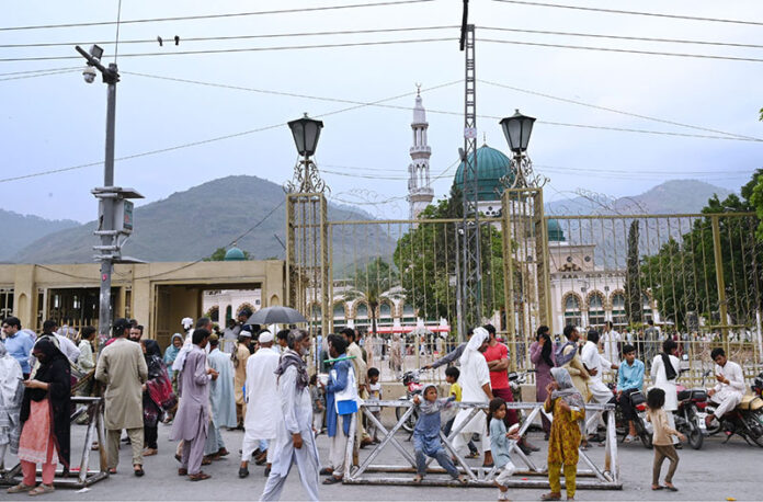 A large crowd gathers at the main entry gate of Shrine Bari Imam in the Federal Capital