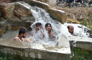 People bathing in running tub well to get relief from scorching hot weather in the city