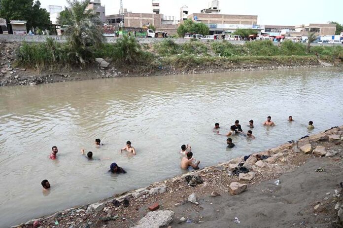 People bathing in running tub well to get relief from scorching hot weather in the city