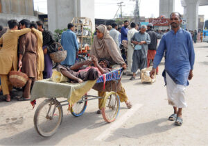 young girl pushes a wheel stretcher carrying a disabled beggar, as they seek mercy from the passersby on a busy city street.