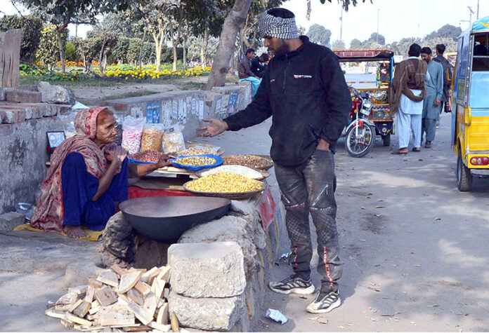 An aged woman sells gram and maize grains roasted on a clay stove in at Shahdra Morr roadside stop