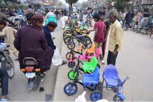 Peoples selecting and purchasing toy bicycles from vendor on the footpath at Latifabad.