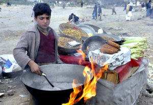 A young vendor roasts corn on his handcart to attract customers near Ravi Road.