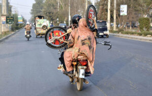 A pillion rider woman carrying a bicycle in a risky way traveling on PIA Road.