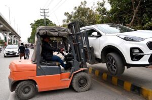 A traffic police official lifting a wrongly parked car with the help of a lifter at Murree Road.