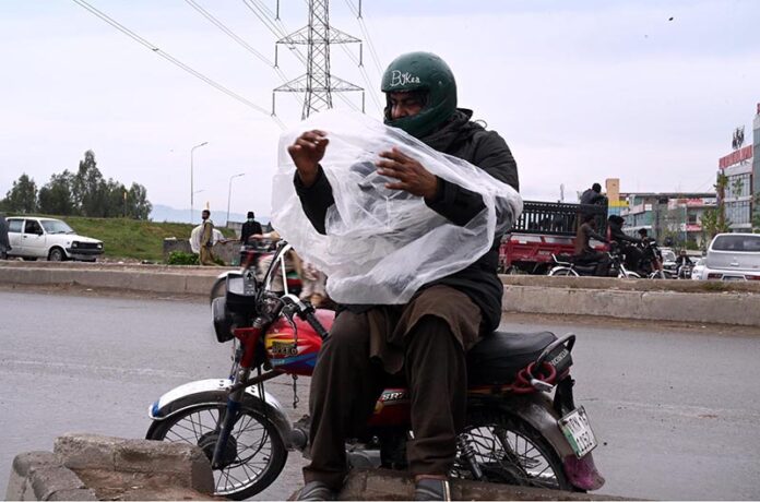 Bike rider is busy wear plastic sheet to cover himself from rain in the Federal Capital