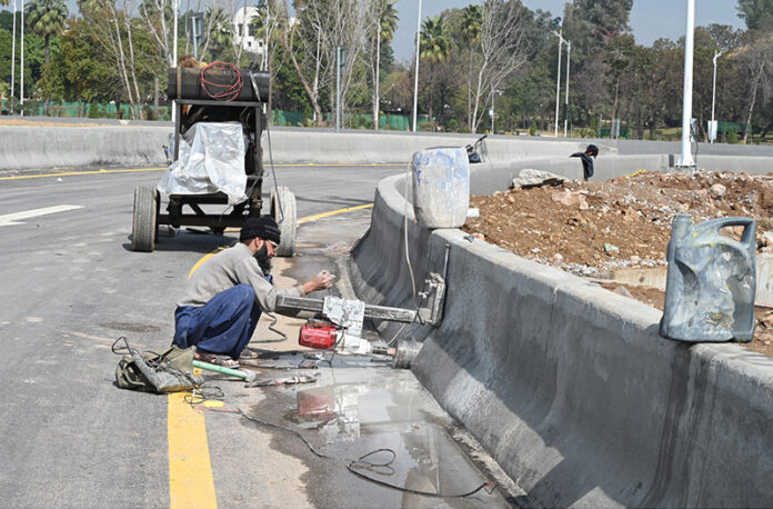 Laborer busy construction work of boundary wall near of roadside greenbelt in the Federal Capital