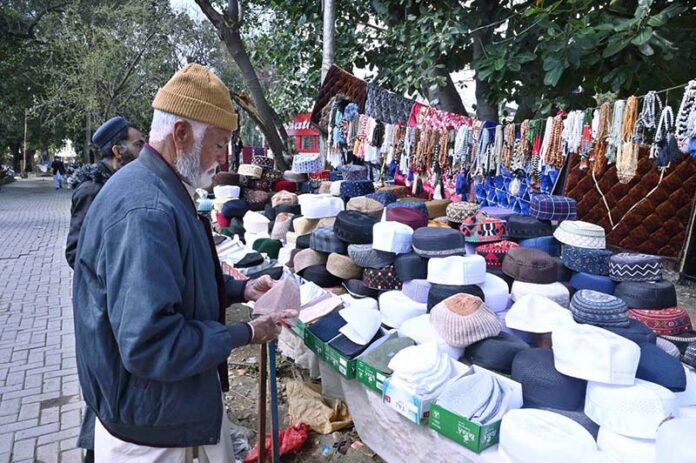 An aged man selects and purchase cap on a roadside stall during holy fasting month of Ramadan at Aabpara in the Federal Capital