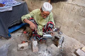 An old worker busy in polishing pots at his workplace near Bandar Road.