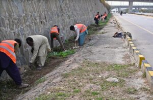 Workers diligently clean the green belt along Srinagar Highway in the Federal Capital for new plantation ahead of the coming spring season.