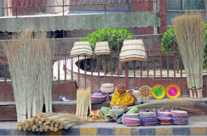 An elderly lady vendor making traditional brush brooms for the customers while sitting at her roadside setup