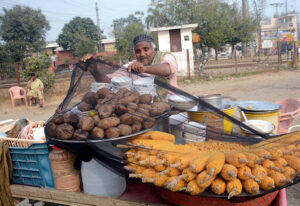 A vendor selling corn and sweet potatoes at roadside setup.