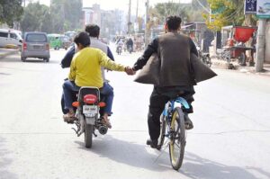 A young boy is helping a cyclist by holding his hand while sitting on the rear seat of a motorcycle.