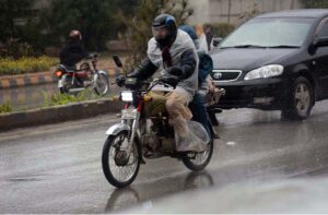 A motorcyclist rides through the city under a plastic sheet, shielding from the heavy rain in the provincial capital.