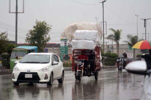 A motorcyclist rides through the city under a plastic sheet, shielding from the heavy rain in the provincial capital.