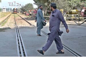 It is an extremely dangerous scene as two people are crossing the railway tracks while a train is approaching from behind, the authorities must intervene to prevent an accident if it occur.