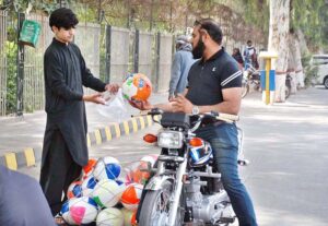 A young vendor selling football to motorcyclists at his roadside stall.