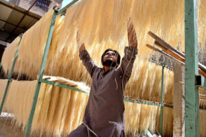 A laborer is hanging and arranging vermicelli (seviyan) to dry after preparing it, as demand has increased during Eidul Fitr.