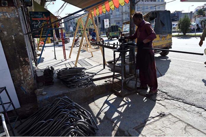 A worker skillfully bends iron pipes outside his shop to make chairs