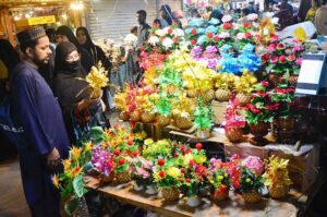 A couple selects colorful artificial flowers from a vendor stall at the local market.