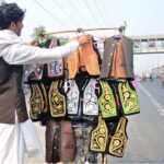 A vendor arranging and displaying traditional waist-coats for children to attract the customers along Gujumta Road