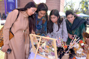 Women look at handmade item on display at a stall in Al-Hamr Hall on the occasion of International Women's Day.