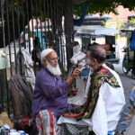 A barber serves a customer at his roadside setup in the Provincial Capital.