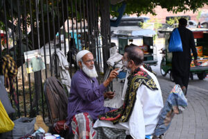 A barber serves a customer at his roadside setup in the Provincial Capital.